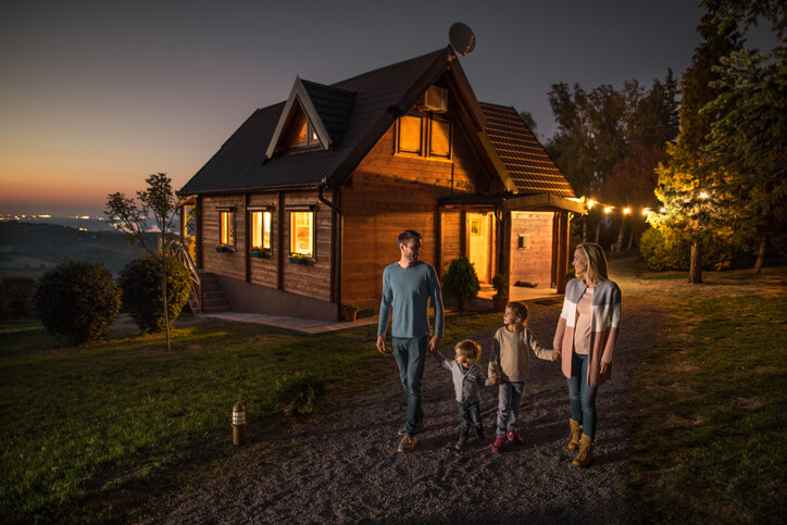 Young smiling parents talking while holding hands with their children and walking in nature in the evening.